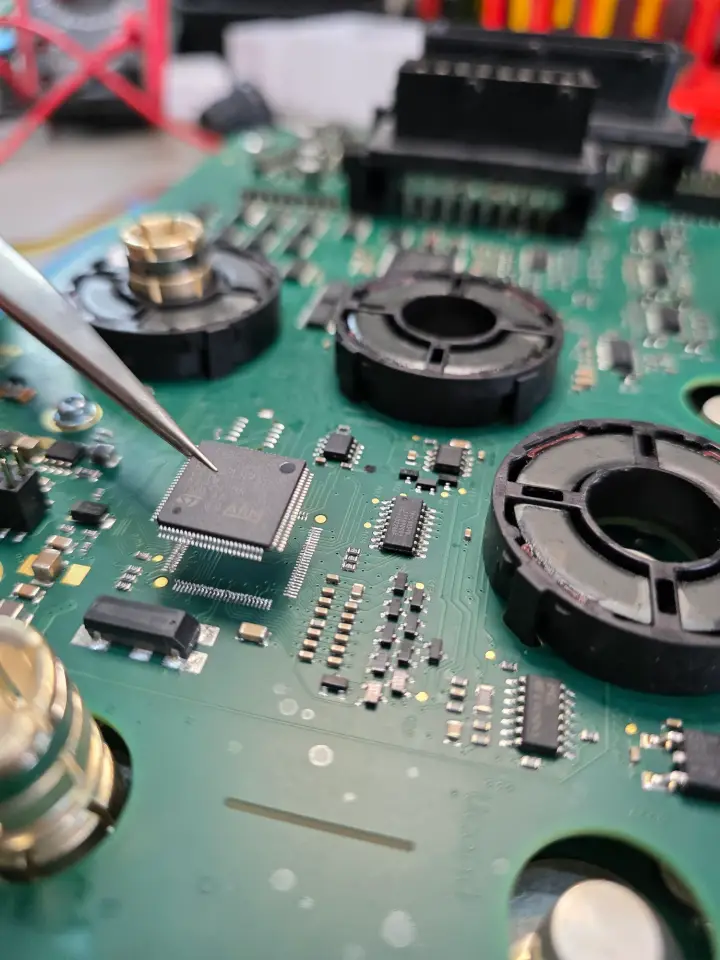 Placa de un controlador con componentes de montaje superficial, trabajada con pinza